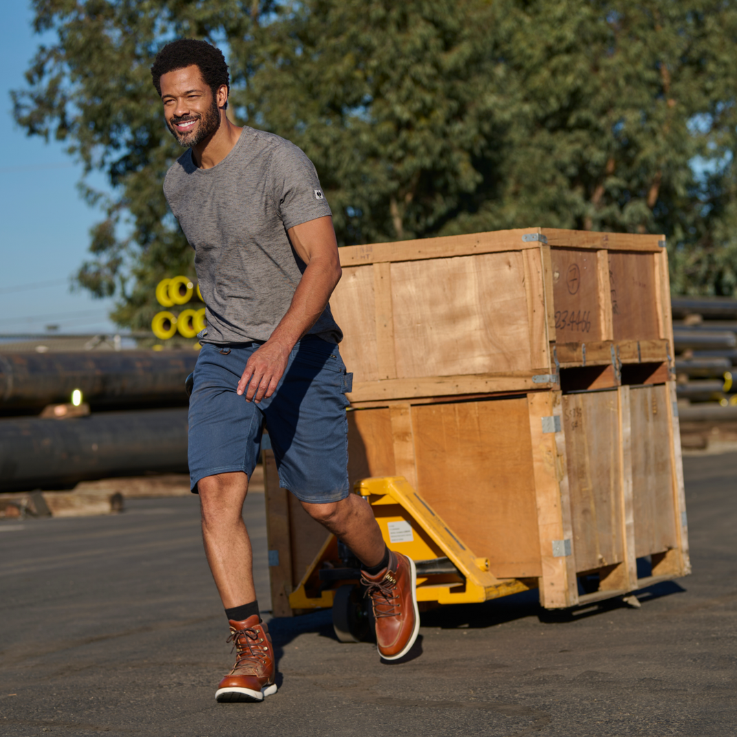 Man walking past wooden crates in an outdoor setting with trees in the background