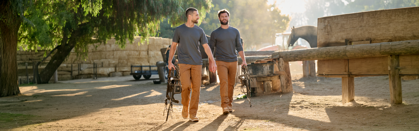 Two men walking with a horse saddle in their hands in a farm environment
