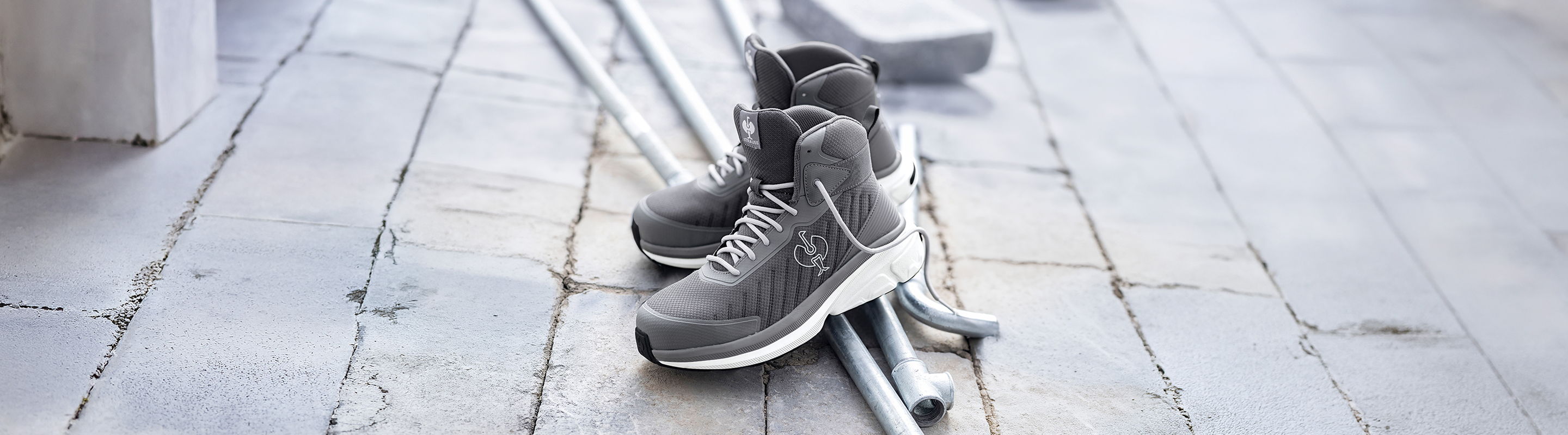 A pair of grey work boots on a concrete floor and metal pipes