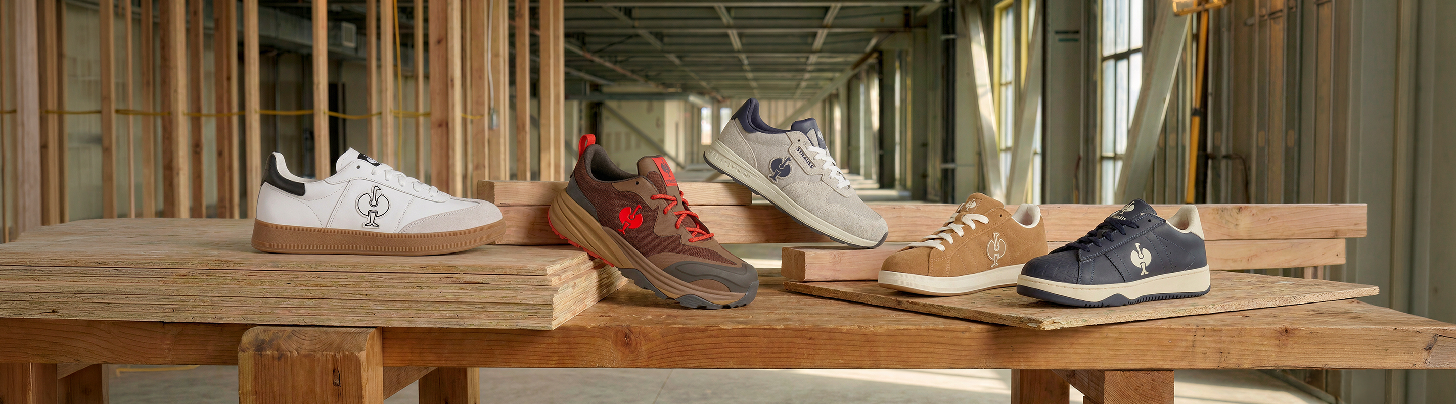 Five pairs of sneakers in various colors are displayed on wooden boards inside a building under construction, showing different styles and materials.