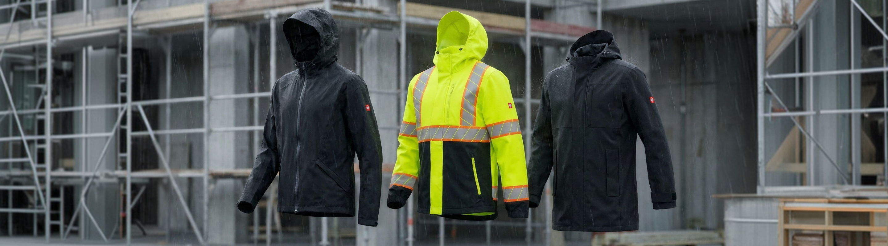Three hooded jackets, two black and one bright yellow with reflective stripes, are displayed in front of a construction site in the rain.