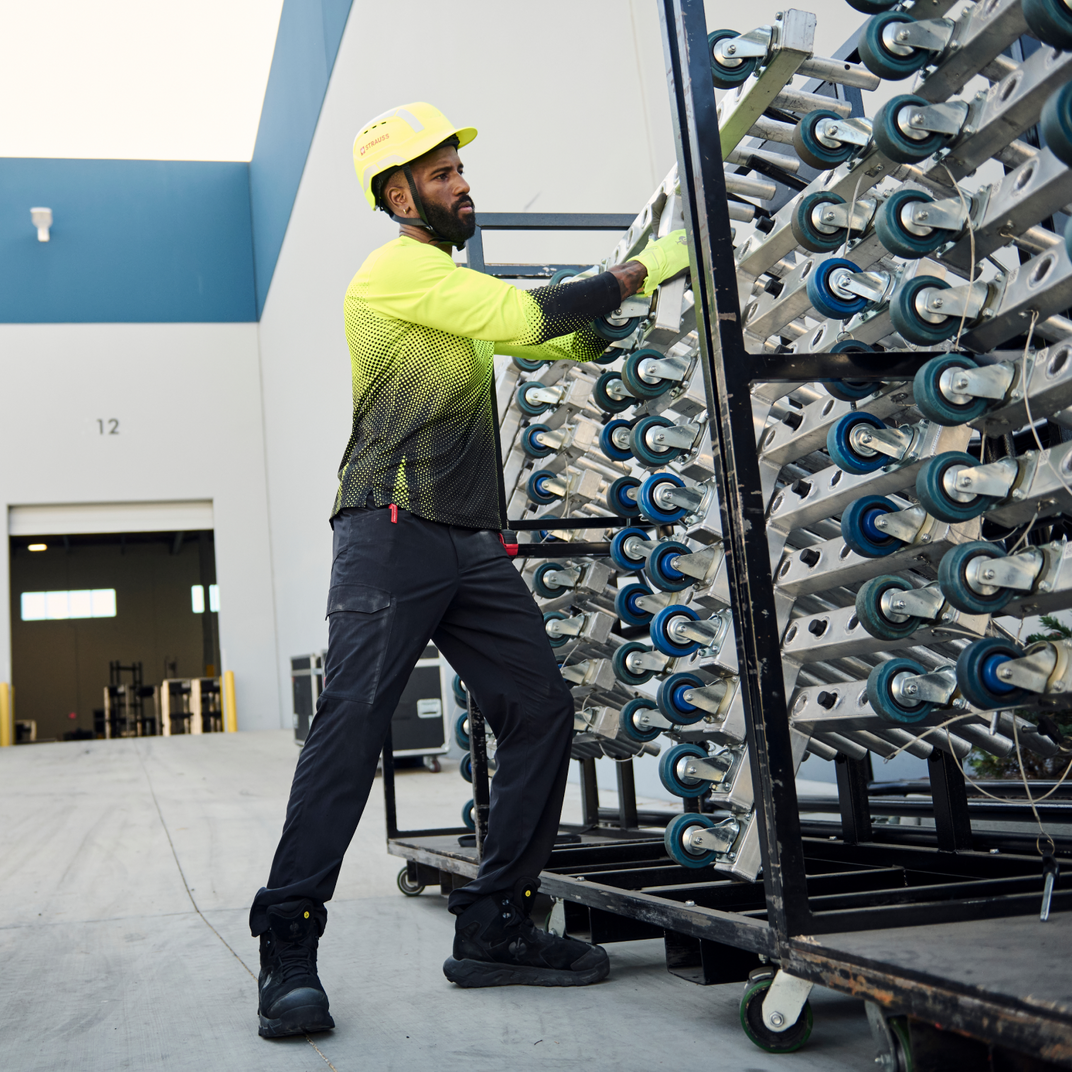 Man in safety gear handling a large metal rack with wheels in an industrial setting