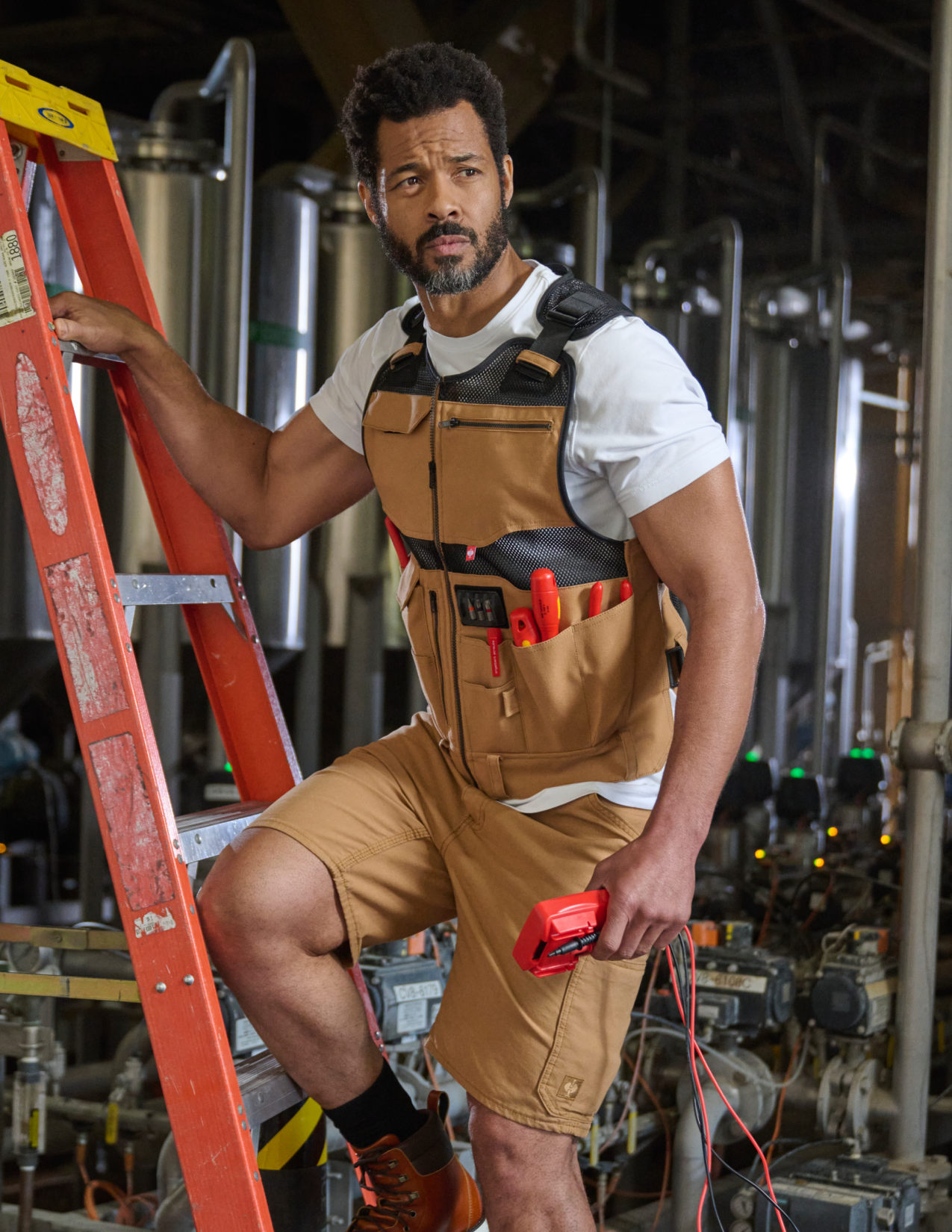 Man in a brown tool vest with tools in a industrial setting