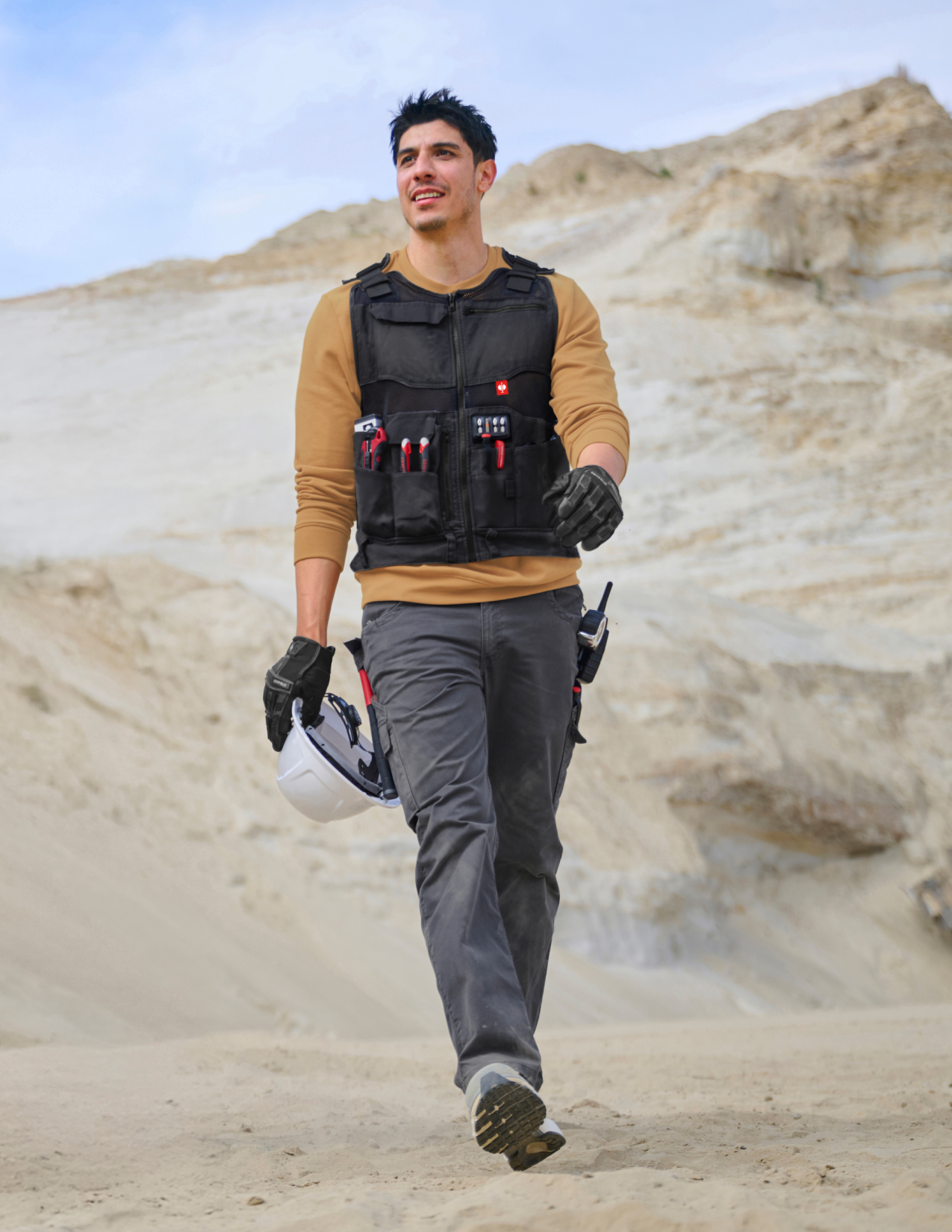 Person wearing a black tool vest with equipment in a desert setting