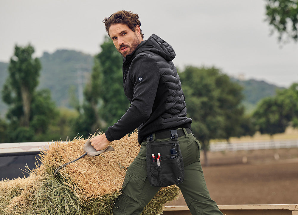 Man carries a bale of hay in a jacket and pants from the Motion Ten collection