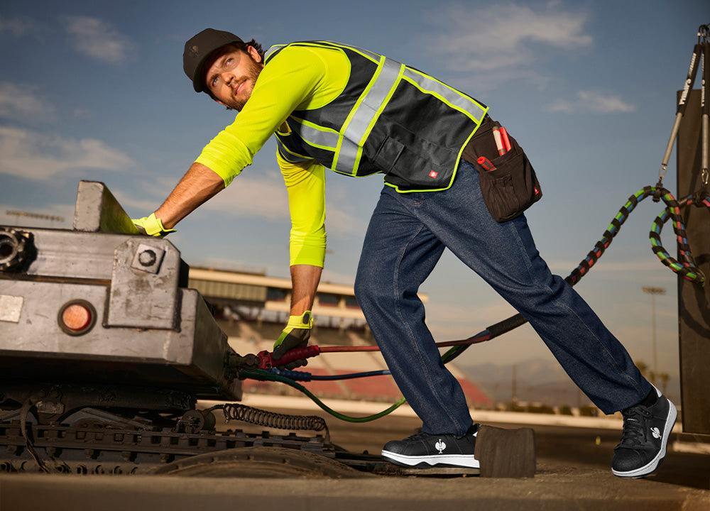 A man operates equipment in a high visibility shirt and vest.