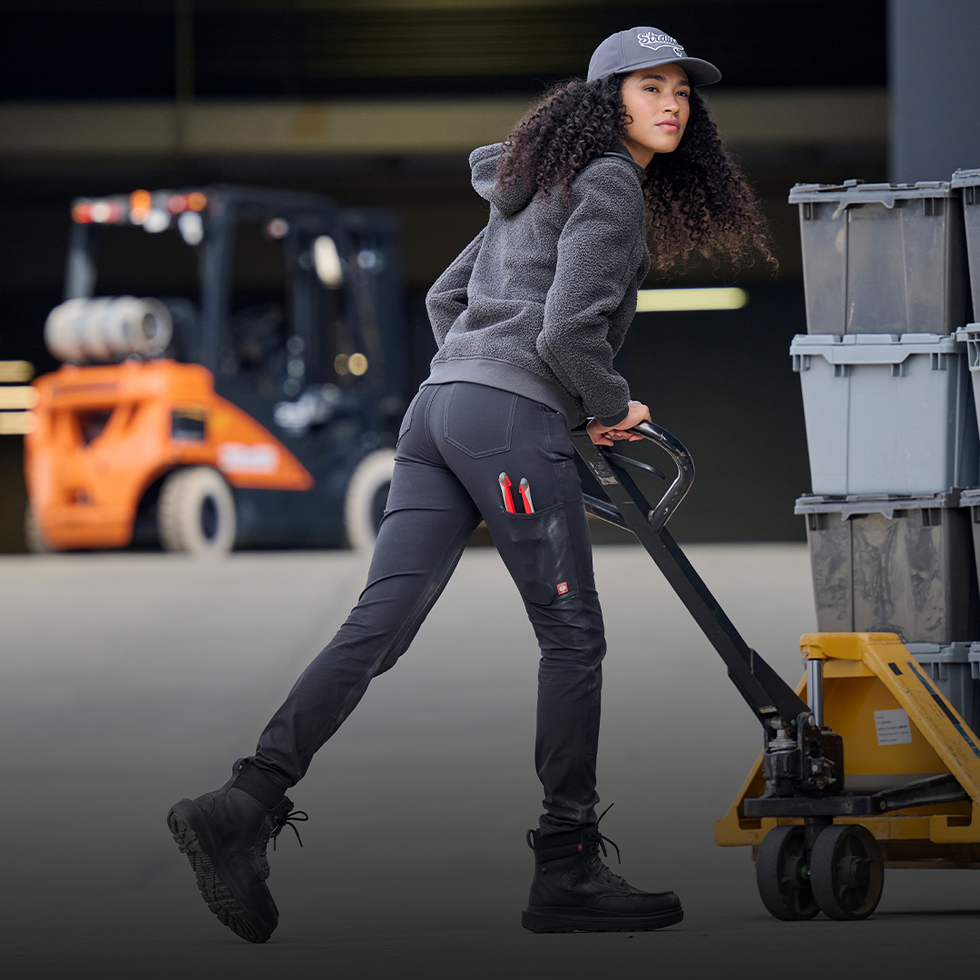 Person using a pallet jack with a forklift in the background