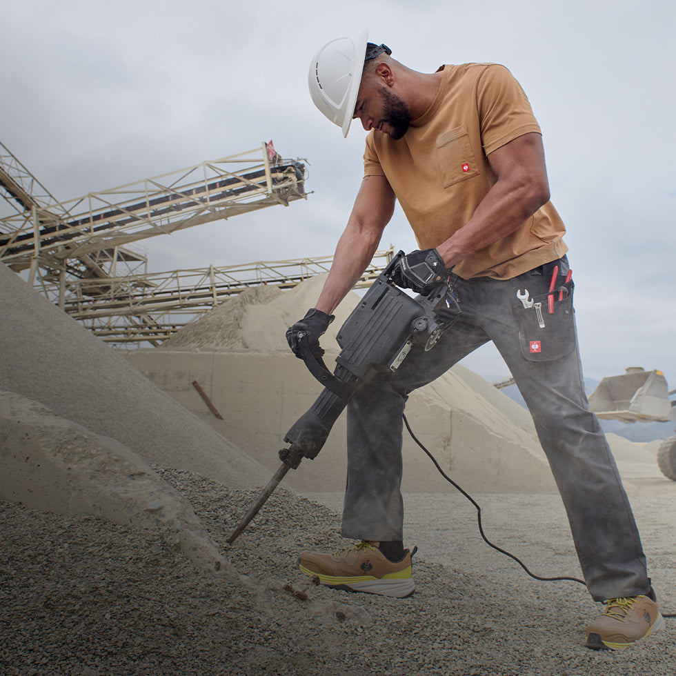 Person using a large tool on a construction site with equipment and sky in the background